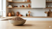 Whole coriander seeds in a ceramic bowl on a wooden kitchen surface, showing natural texture and freshness